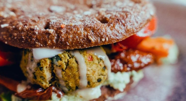 Gros plan sur un burger garni de falafels sauce blanche tomates sechees et carottes