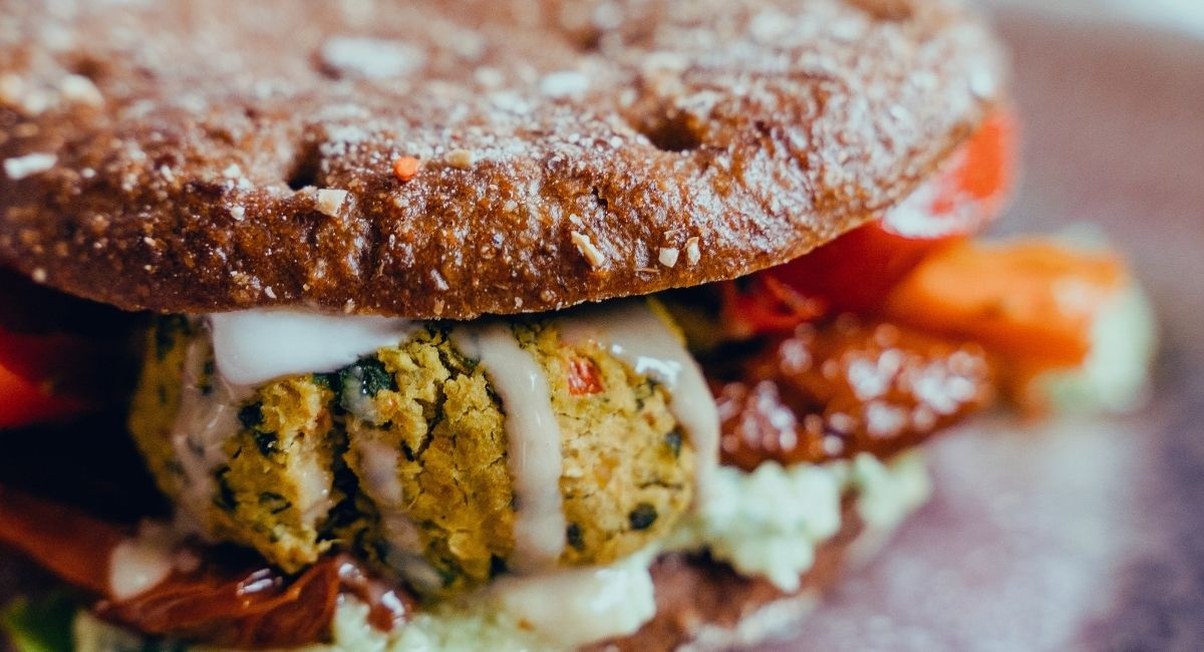Gros plan sur un burger garni de falafels sauce blanche tomates sechees et carottes
