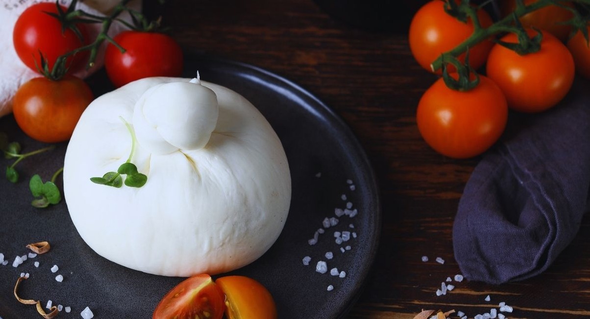 Boule de burrata fraiche posee sur une assiette sombre entouree de tomates cerises