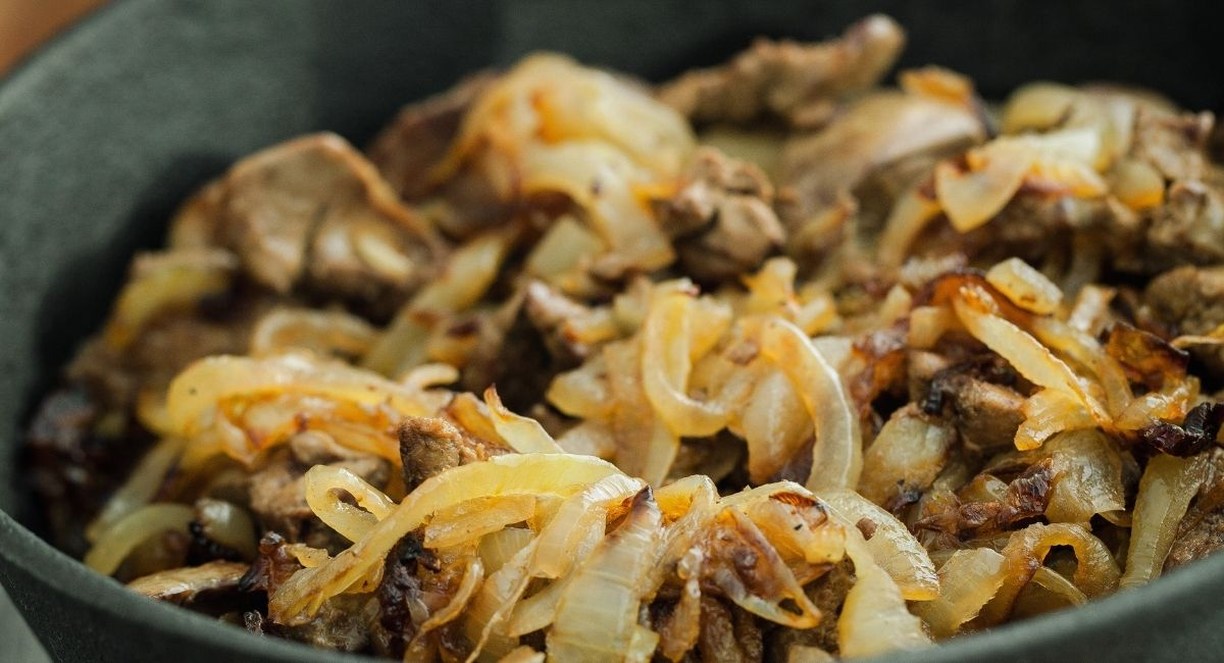 Morceaux de foie poeles avec des oignons fondus dans une poele en fonte