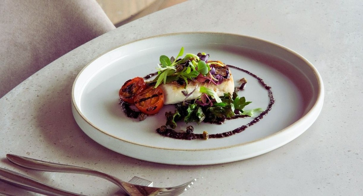 Assiette dressee avec un pave de poisson tomates confites pousses et sauce sombre