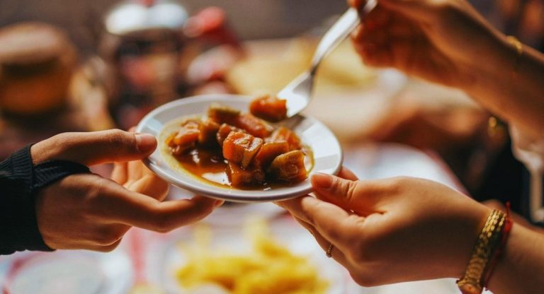 Deux convives se passent une petite assiette de legumes mijotes autour d une table