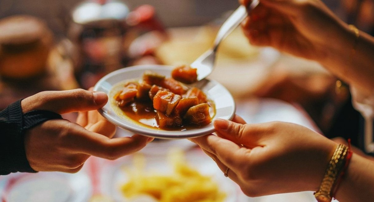 Deux convives se passent une petite assiette de legumes mijotes autour d une table