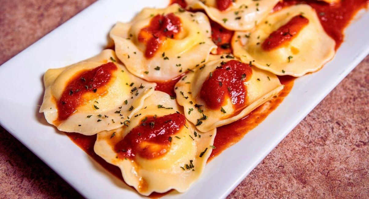 Raviolis frais nappes de sauce tomate et de persil sur une assiette rectangulaire blanche