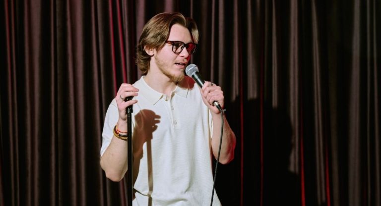 Humoriste au micro devant un rideau rouge sur une scene de stand-up