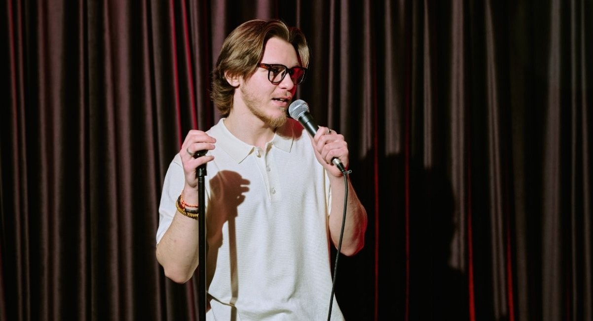 Humoriste au micro devant un rideau rouge sur une scene de stand-up