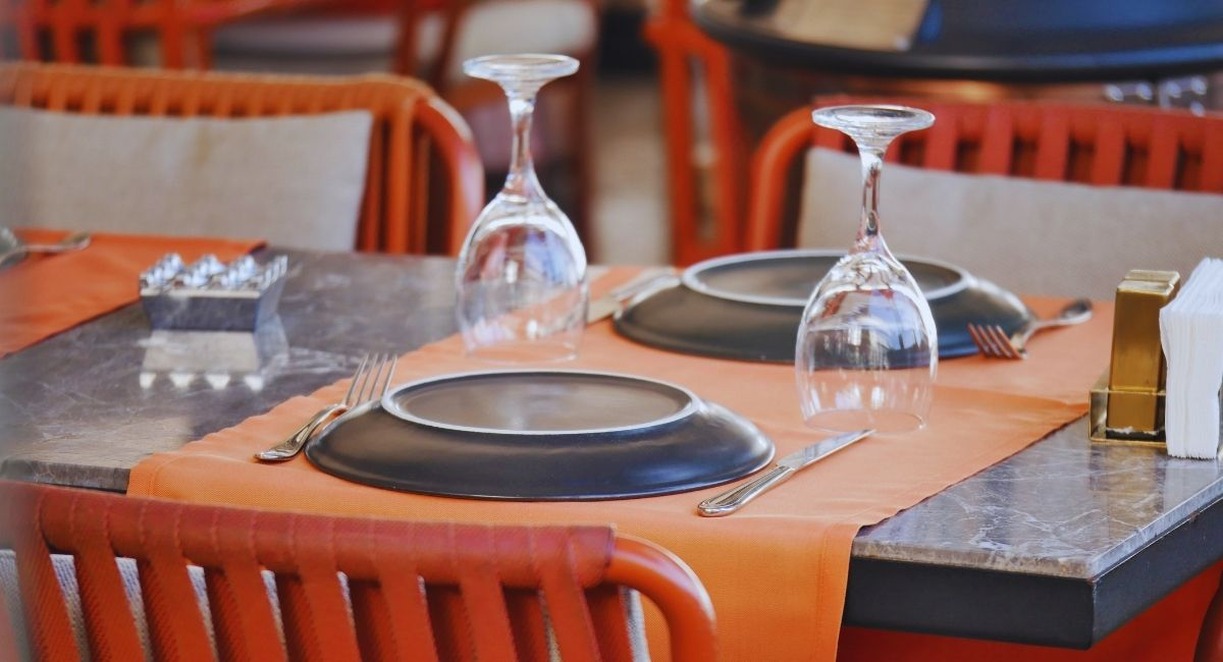 Table de restaurant dressee avec assiettes noires verres retournes et chemin de table orange