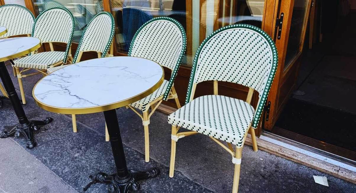 Chaises de bistrot en rotin vert et blanc et tables rondes en marbre sur un trottoir